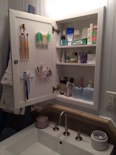 an open medicine cabinet in the corner of a bathroom sink with toothbrushes and other hygiene products