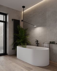 a large white bath tub sitting next to a plant in a bathroom on top of a hard wood floor