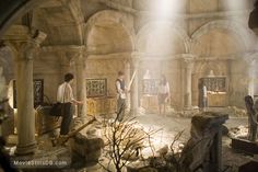 people standing around in an old building with stone arches and pillars, while the light shines on them