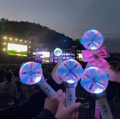 people are holding up lights in front of an outdoor stage at night with the lights turned on