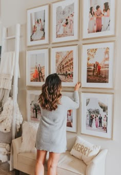 a woman standing in front of a wall with pictures on it and holding her hand up