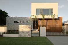 a modern house with stone walls and wooden fenced in area next to the grass