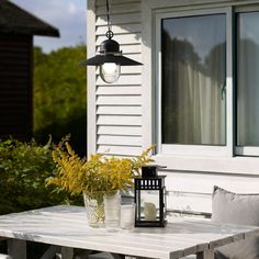 an outdoor table with a lantern and flowers on it in front of a white house