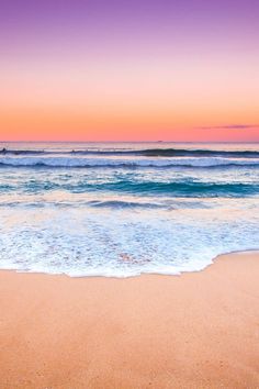 an ocean beach with waves coming in to shore and people on the water at sunset