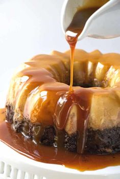 someone drizzling caramel sauce over a chocolate cake on a white plate