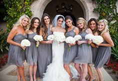 a group of women standing next to each other in front of a doorway holding bouquets