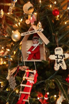 a christmas tree with an elf in a house ornament hanging from it's side