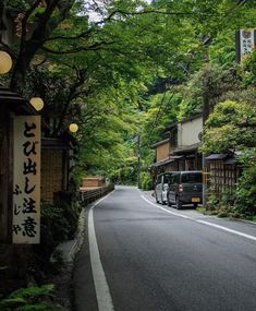 a bus driving down a street next to lush green trees and lanterns hanging from the ceiling