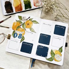 an open planner with lemons and leaves on it next to some paintbrushes