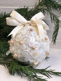 an ornament made out of buttons and pine needles with a bow on top