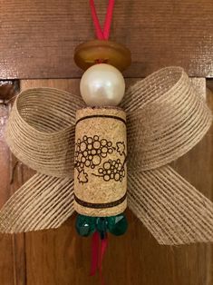 a wine cork angel ornament hanging on a wooden door with pearls and ribbon