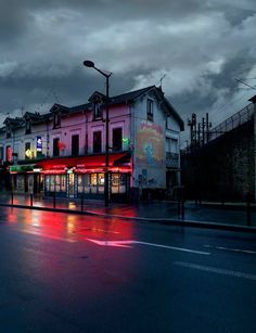 an empty city street at night with the lights on and dark clouds in the background