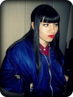 a woman with long black hair wearing a blue jacket and red lipstick is posing for the camera