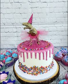 a birthday cake decorated with sprinkles and a gold dinosaur figure on top