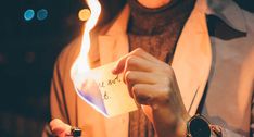 a person holding a piece of paper with writing on it in front of a lit candle