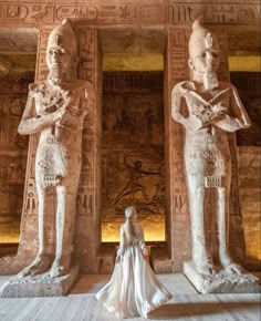 a woman standing next to two statues in front of an egyptian wallpapered room