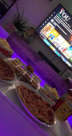 pizzas and chips are on the table in front of a television set with purple lighting