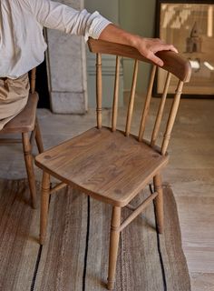 a wooden chair sitting on top of a rug next to a person's hand