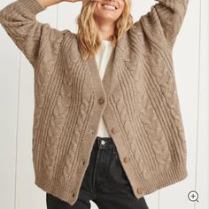 a woman wearing a brown cardigan sweater and black jeans with her hands on her head