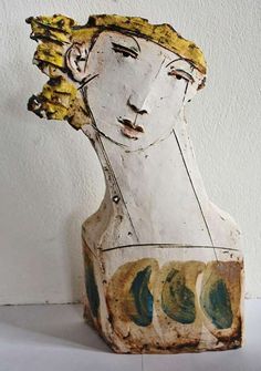 a wooden sculpture with multiple faces on it's face and hair blowing in the wind