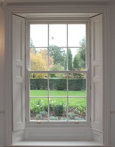 an open window in a white room with green grass and trees behind the windowsill