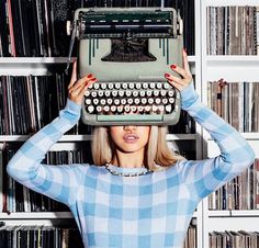 a woman holding an old fashioned typewriter over her head in front of a bookcase