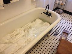 a white bath tub sitting next to a wooden table in a bathroom with black and white tile