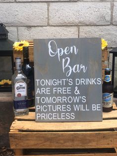 an open bar sign sitting on top of a wooden table next to bottles of alcohol