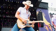 a man with a cowboy hat playing an electric guitar in front of a crowd at a music festival