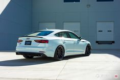 the rear end of a white car parked in front of a garage door on a sunny day