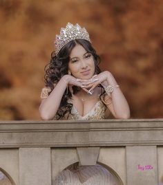 a woman wearing a tiara and posing on a ledge with her hands behind her head