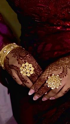 two hands with henna tattoos and gold jewelry on their palms, both holding onto each other