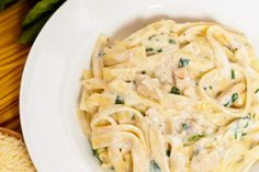 a white plate topped with pasta covered in chicken and sauce next to breadsticks