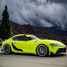 a bright yellow sports car parked on the side of a road with mountains in the background