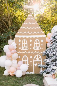 a gingerbread house with balloons in front of it and a christmas tree next to it