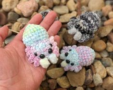 someone is holding two small knitted animals in their hand on some rocks and gravel