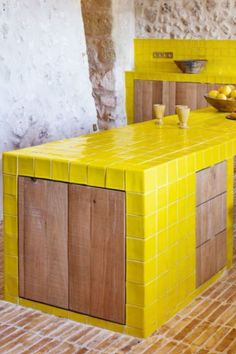 a kitchen with yellow tiles on the counter top and wooden cabinets in front of it