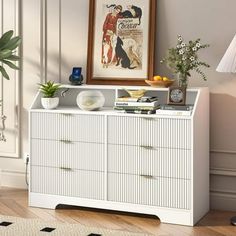 a white dresser sitting in a living room next to a lamp and pictures on the wall