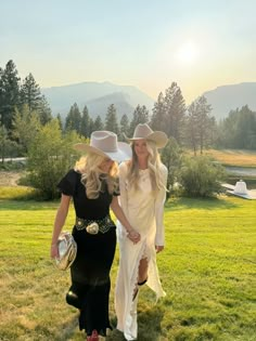 two women in cowboy hats are walking through the grass