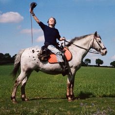 a man riding on the back of a white horse in a green field with blue sky