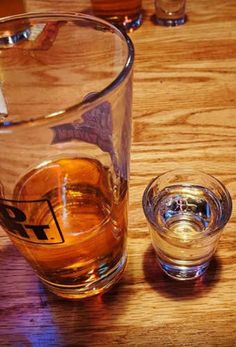 an empty glass sitting on top of a wooden table next to a shot glass filled with liquid