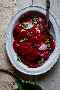 a white bowl filled with beets on top of a table next to a spoon