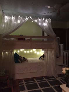 a bunk bed with white curtains and lights on the ceiling above it in a bedroom