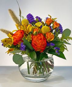 a glass vase filled with lots of colorful flowers and greenery on top of a table