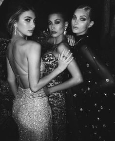 three beautiful women standing next to each other in front of a black and white photo