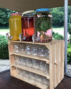 three jars and glasses on top of a wooden shelf