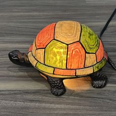 a colorful turtle lamp sitting on top of a wooden table next to a black wire