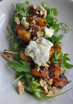 a white plate topped with lots of food on top of green lettuce and nuts