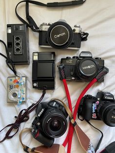 many cameras and accessories are laid out on a white sheet with a red cord attached to the camera