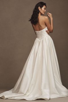 a woman in a white wedding dress with her back turned to the camera and looking at something